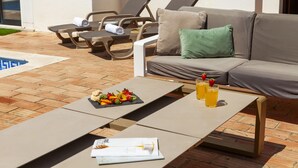 A poolside area with lounge chairs, a sofa, and a table with fruit and drinks. - Villa Bellegarde (Albufeira)