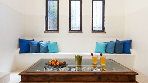 A room with a glass-top table, a bench with blue cushions, and three arched windows with frosted glass. - Villa Bellegarde (Albufeira)