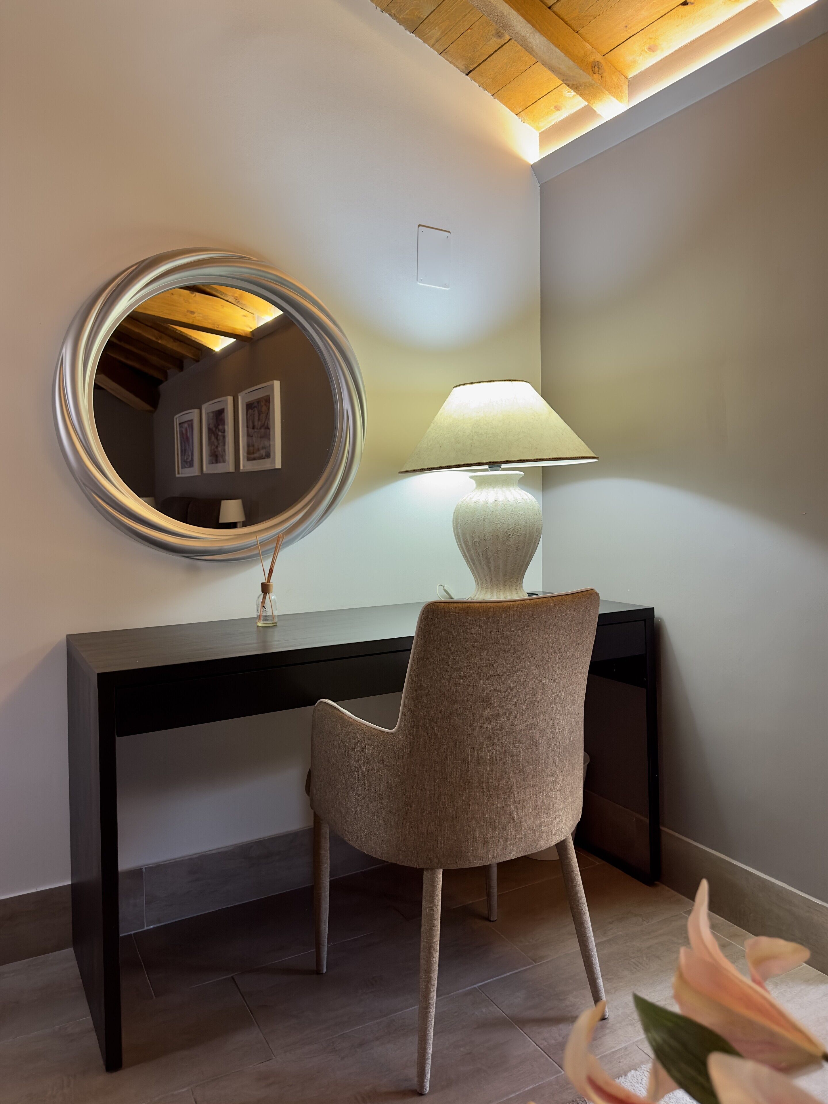 A modern room with a dark console desk, a round mirror, a lamp, and a chair.
