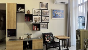 A modern living room with a wooden cabinet, black chair, and a small table. There are framed pictures on the wall and a water dispenser on the right. - Spacious apartment within walking distance of Duomo and Pescheria (Catania)