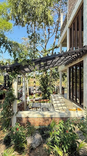 A modern house with a covered patio, stone steps, and a garden with various plants and a rock. - Kawarin River Exclusive Hotel & Resort (Thong Pha Phum)