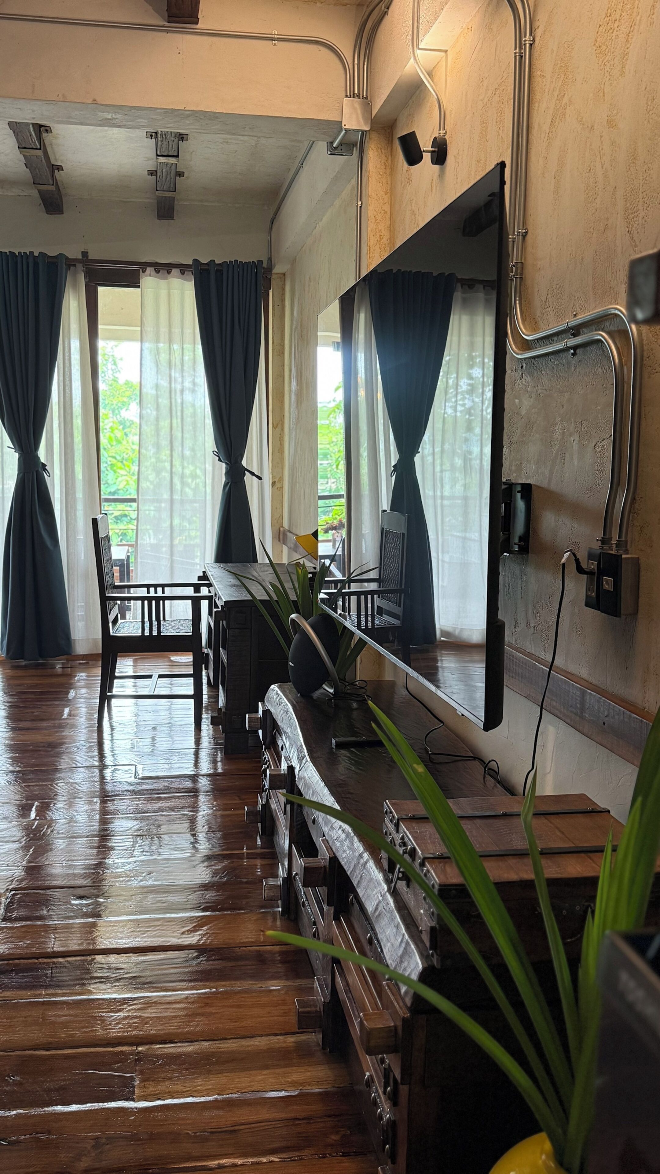 Una habitación con suelo de madera, una mesa, sillas, un espejo y un ventanal con cortinas.