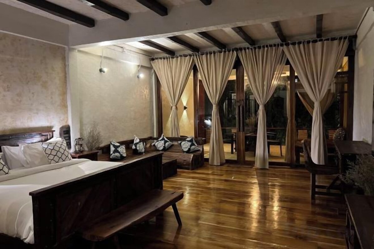 A hotel room with a wooden floor, a large bed, a bench, and curtains.