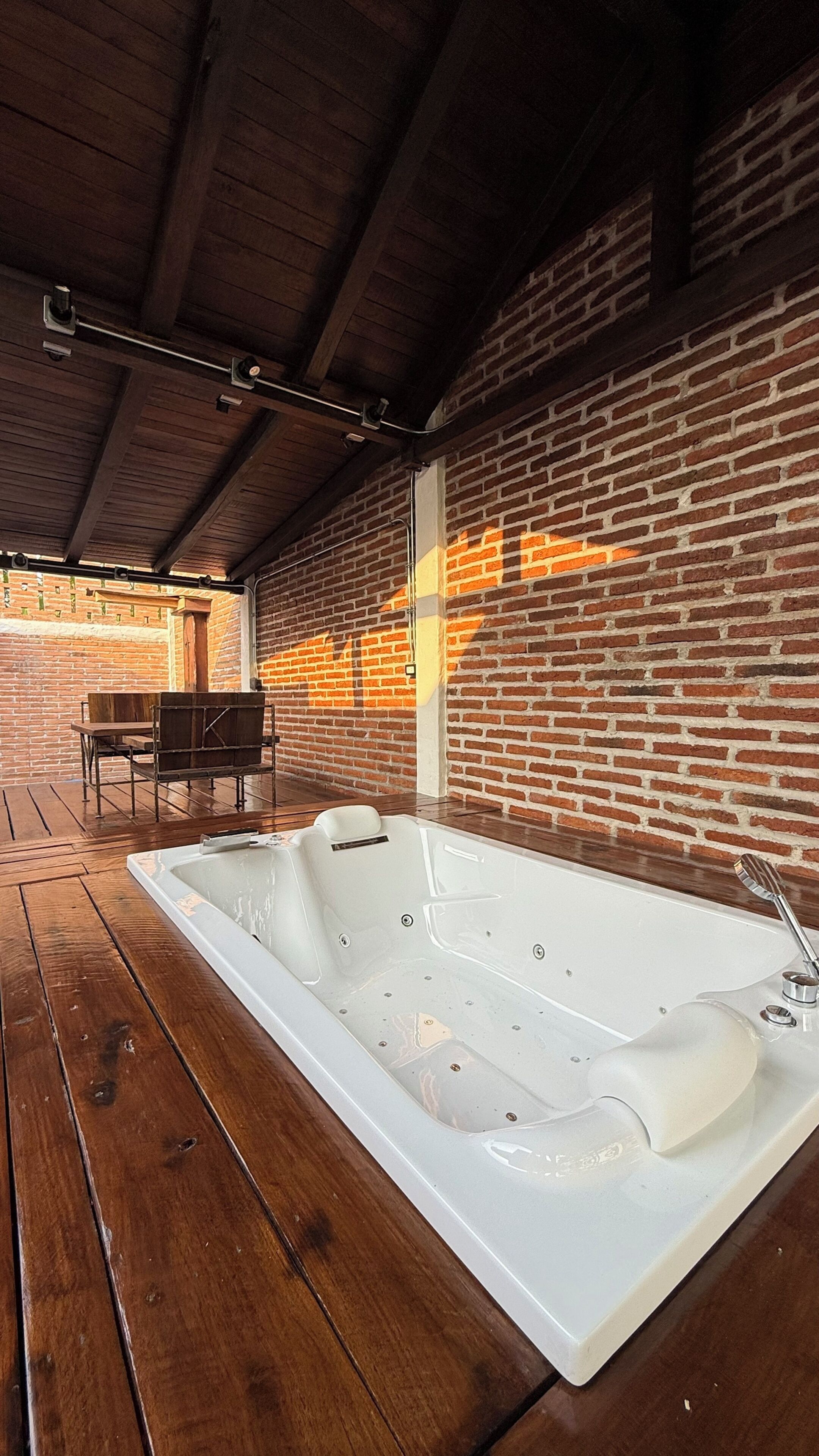 A spa area with a large white bathtub, wooden flooring, and brick walls.