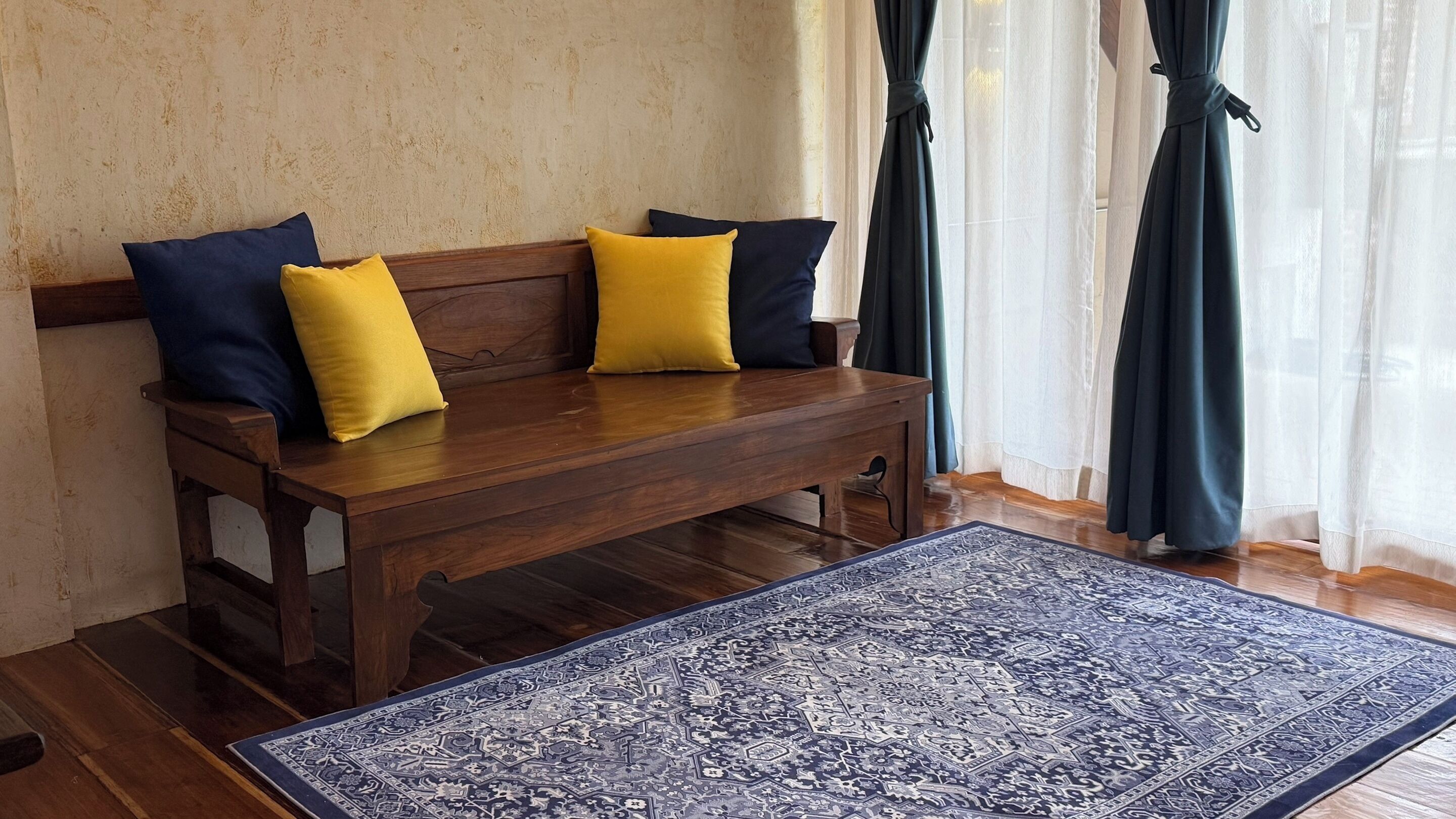 Un banc en bois avec des coussins, un tapis à motifs et des rideaux en voile.