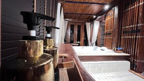 A wooden interior with a bathtub, a wooden bench, and a wall-mounted pump.