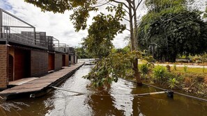 A riverside walkway with a wooden deck, brick walls, and a metal railing. - Kawarin River Exclusive Hotel & Resort (Thong Pha Phum)