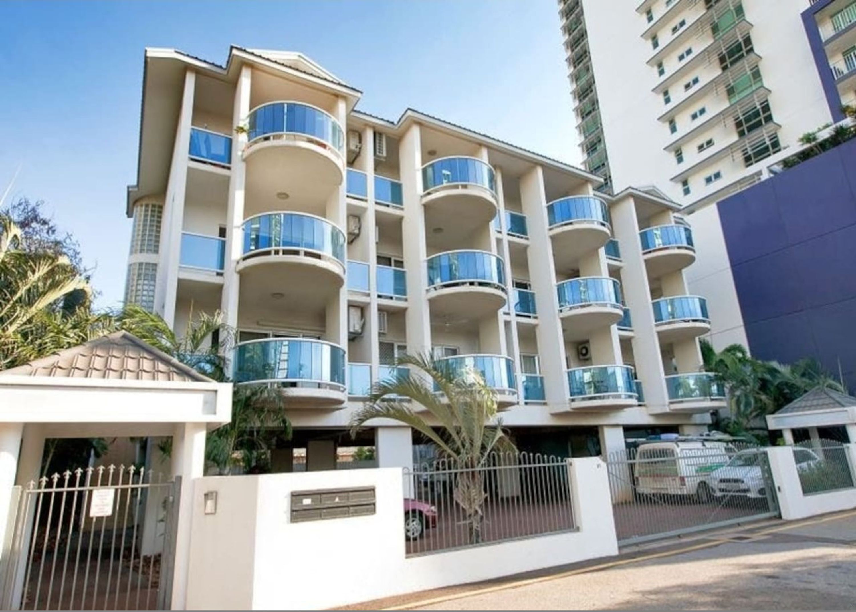A multi-story residential building with balconies, a gated entrance, and a small adjacent structure.