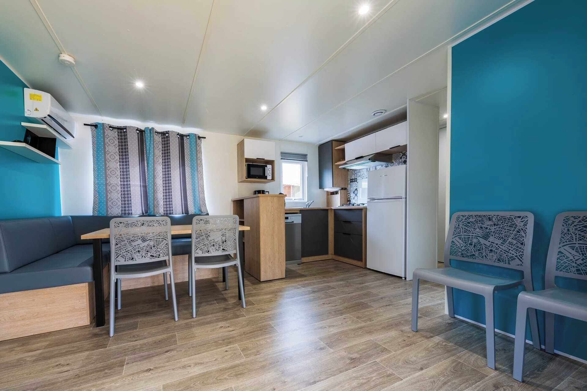 Un espacio habitable compacto con kitchenette, zona de comedor con mesa y sillas, y zona de estar con sofá y sillas.