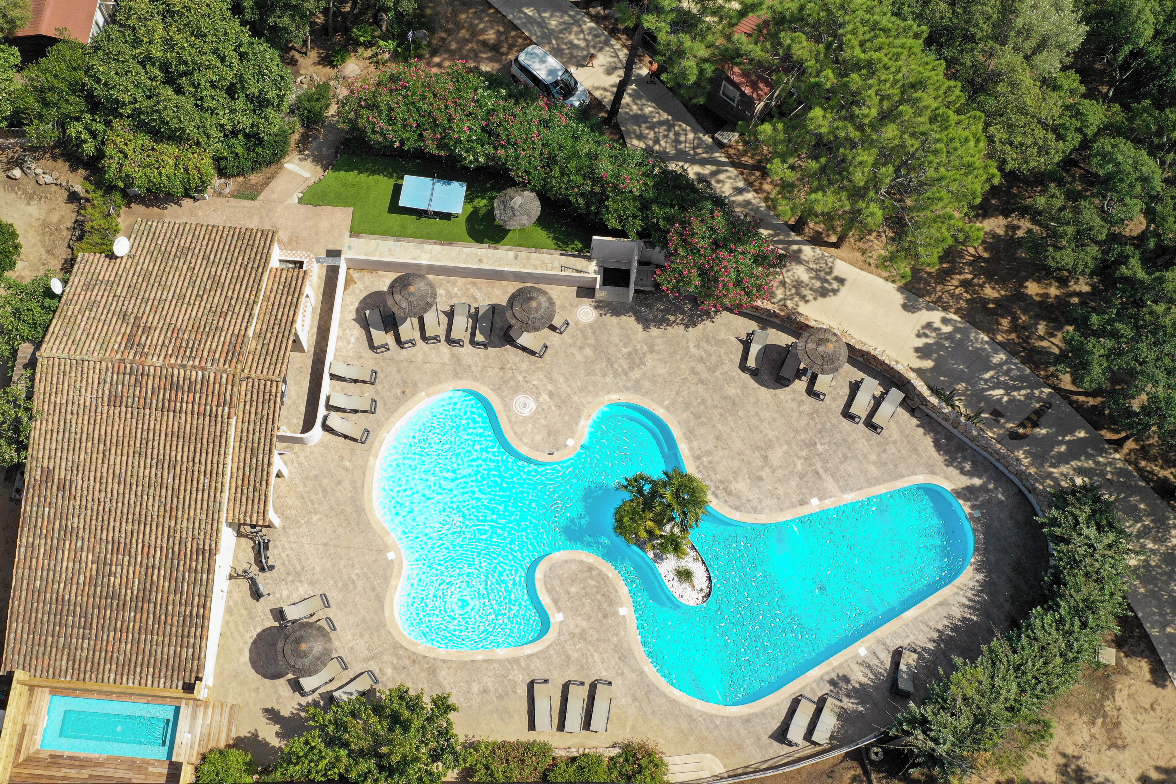 An aerial view of a resort with a swimming pool, lounge chairs, and a small building.