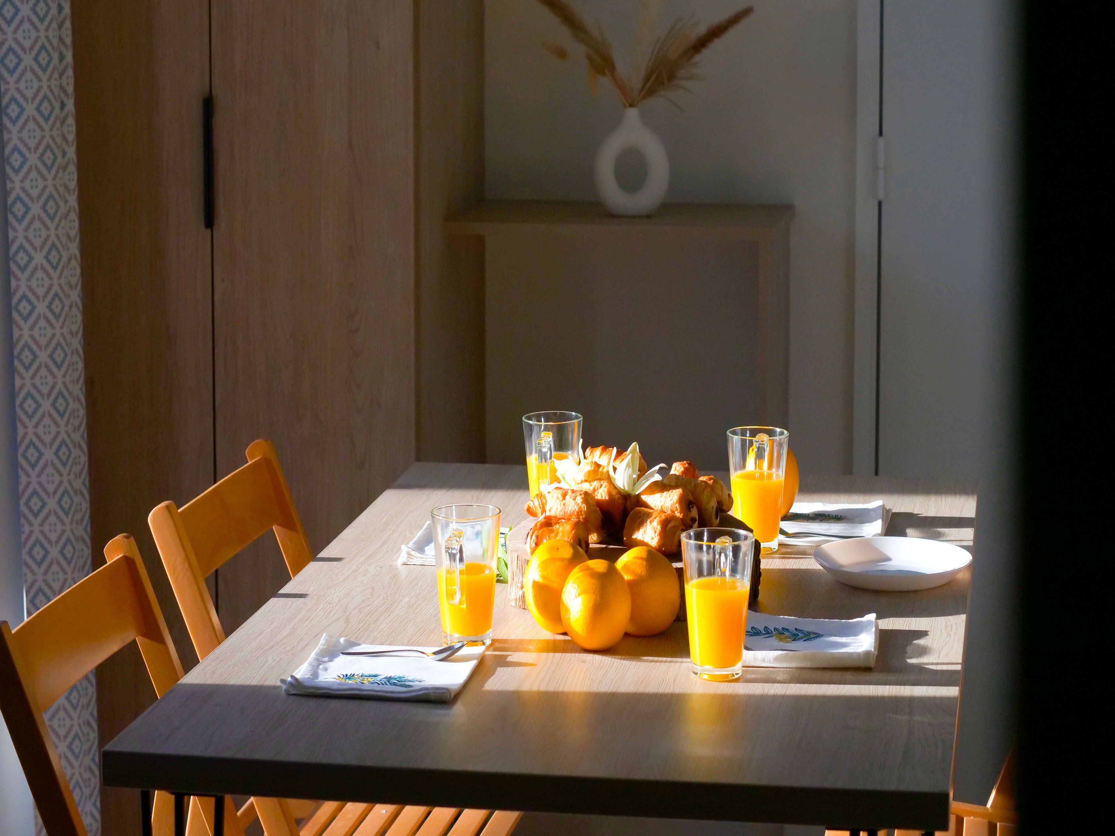 A dining table with chairs, a vase with dried plants, and a plate with food and drinks.