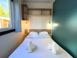 Una cama bien hecha con ropa blanca y toallas, un cabecero con repisas integradas, lámparas de noche y una ventana con cortinas estampadas.