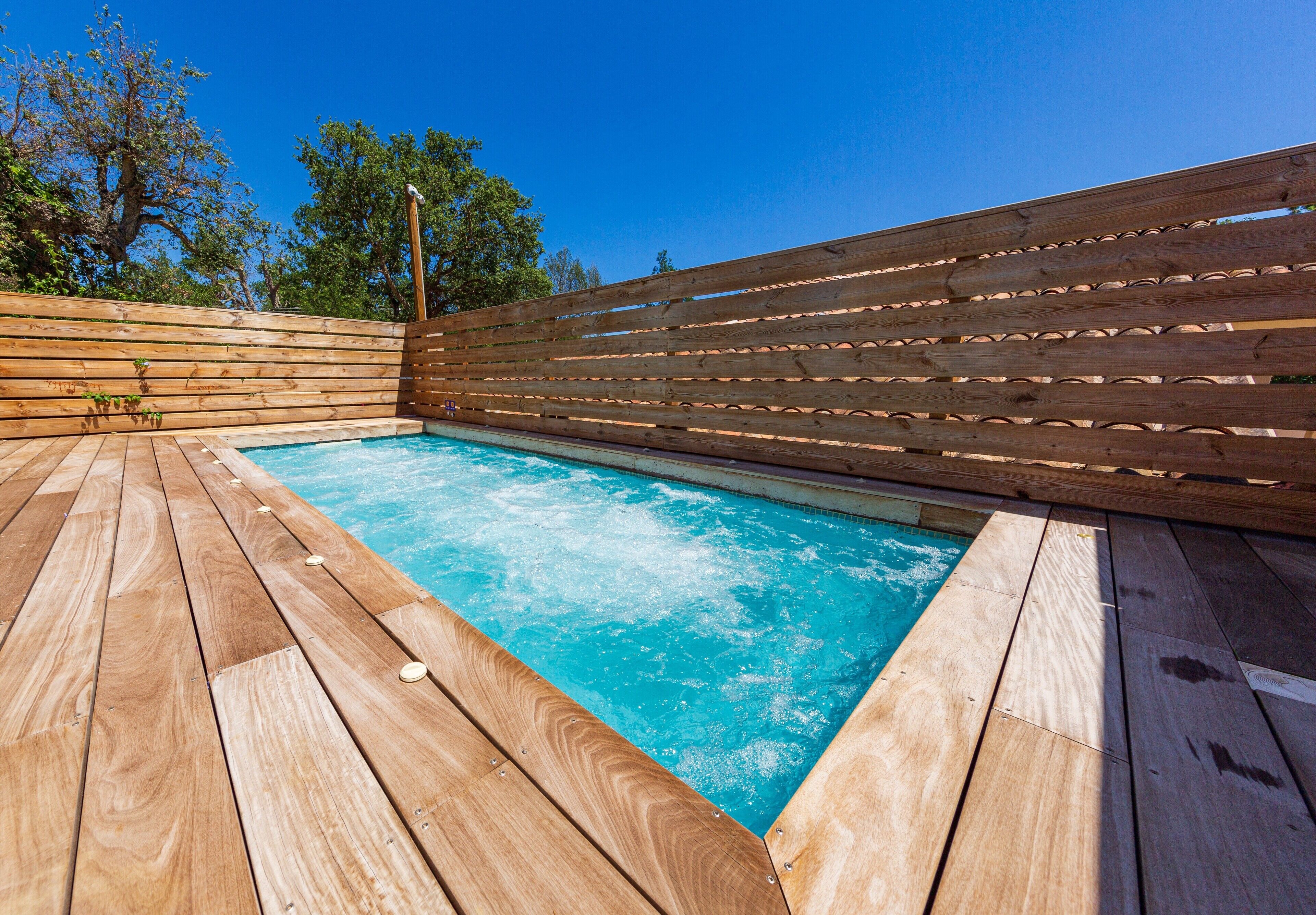 A wooden deck surrounding a swimming pool with a wooden fence and trees in the background.