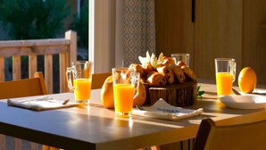 A breakfast setting with croissants, orange juice, and a fruit bowl on a wooden table.