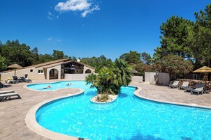 Una piscina con sillas de descanso, un edificio de tejado con baldosas y árboles al fondo.