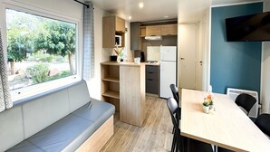 A modern kitchen with a built-in stove, white refrigerator, and wooden cabinets. There is a dining table with chairs and a bench with a view of the outdoors.
