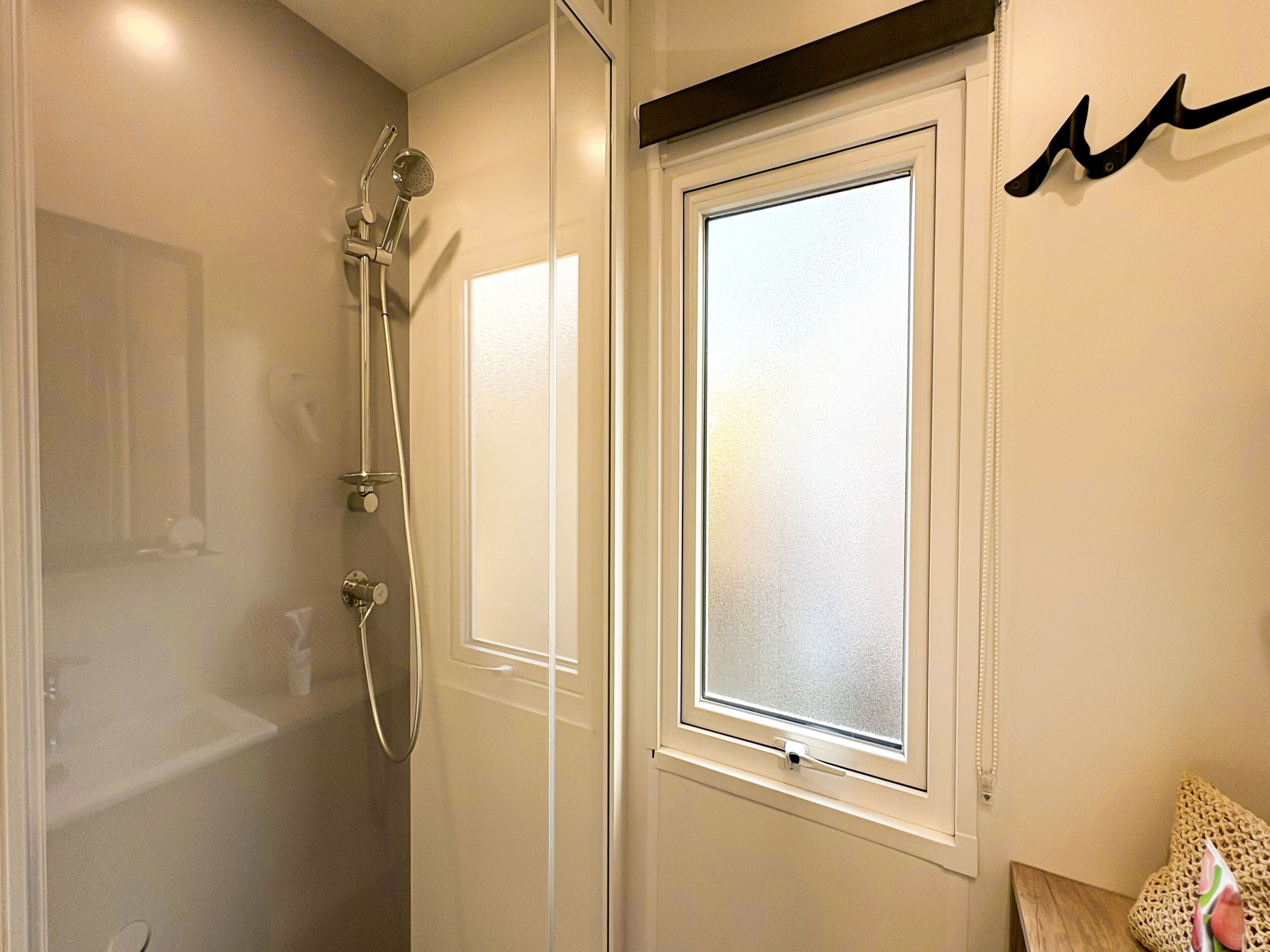 A bathroom with a glass shower enclosure, a white door, and a frosted window.
