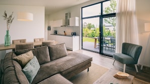 En moderne stue med sofa, spisebord og et køkken i baggrunden.