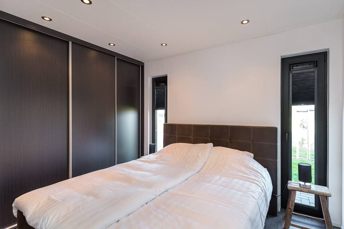 A bedroom with a large bed, dark wooden wardrobe, and a window with a view of greenery.