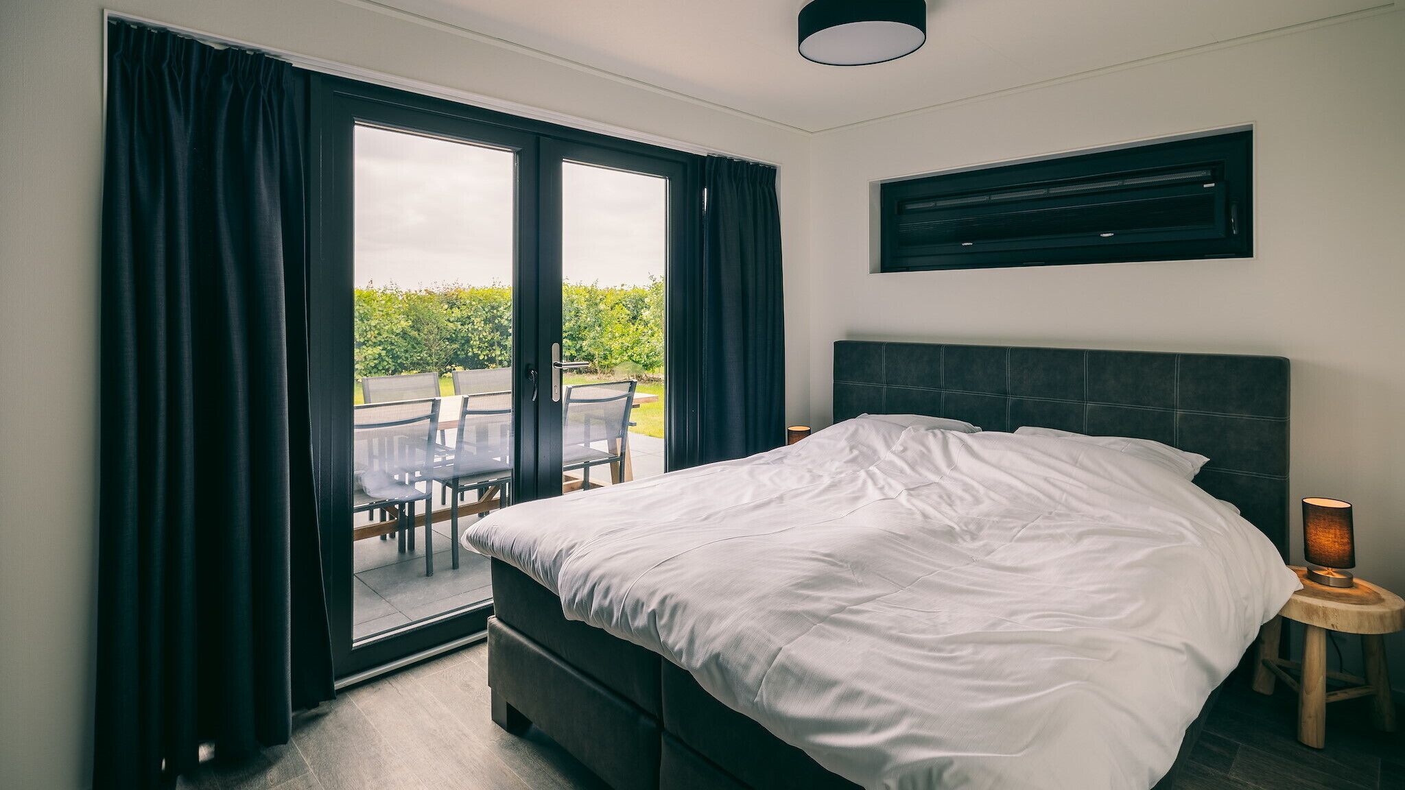 A bedroom with a bed, a window with curtains, a ceiling light, and a wall-mounted air conditioning unit.