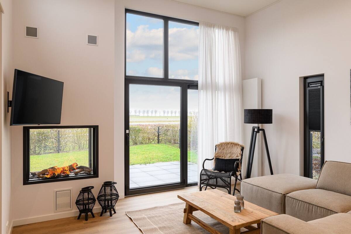 A modern living room with a large sliding glass door, a flat-screen TV, a sofa, a coffee table, and a floor lamp.