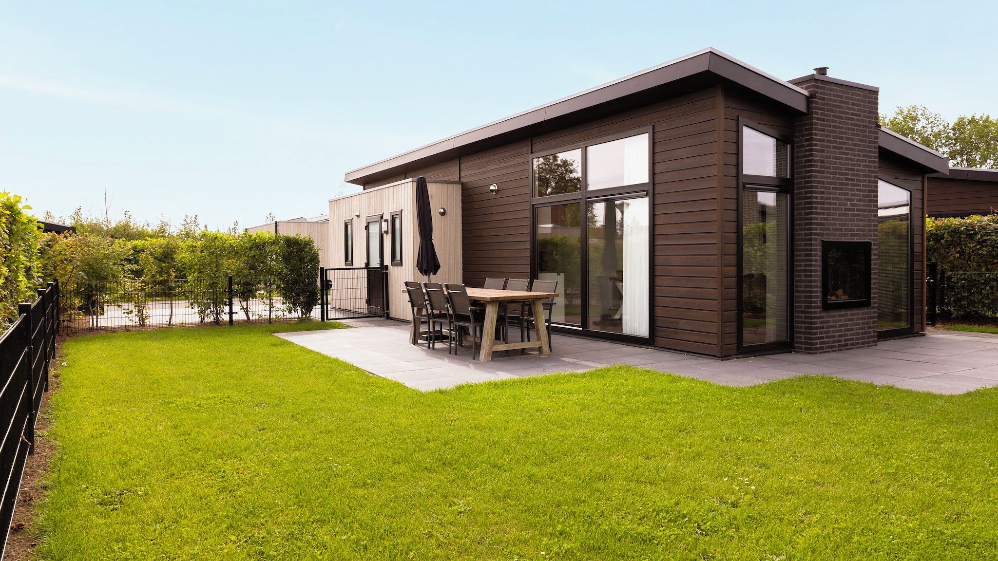 Une maison moderne à deux étages, dotée d’un patio, d’un coin repas et d’une grande porte vitrée.