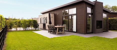 Une maison moderne à deux étages, dotée d’un patio, d’un coin repas et d’une grande porte vitrée.