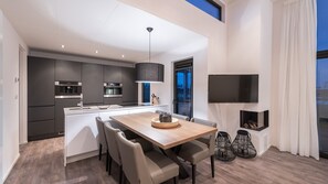 A modern kitchen with dark cabinetry, a central island, and a dining area with a wooden table and chairs. - Summio Vakantiepark Zeedijk (Herkingen)