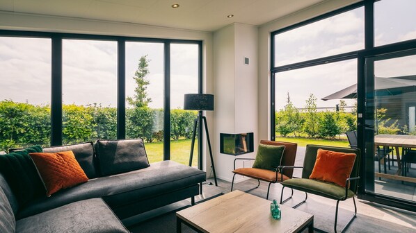 A modern living room with large windows, a sofa, chairs, a coffee table, and a floor lamp. - Summio Vakantiepark Zeedijk (Herkingen)