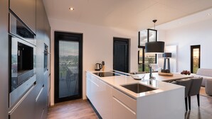 Et moderne køkken med en central ø, integrerede hårde hvidevarer og store vinduer med udsigt til omgivelserne.