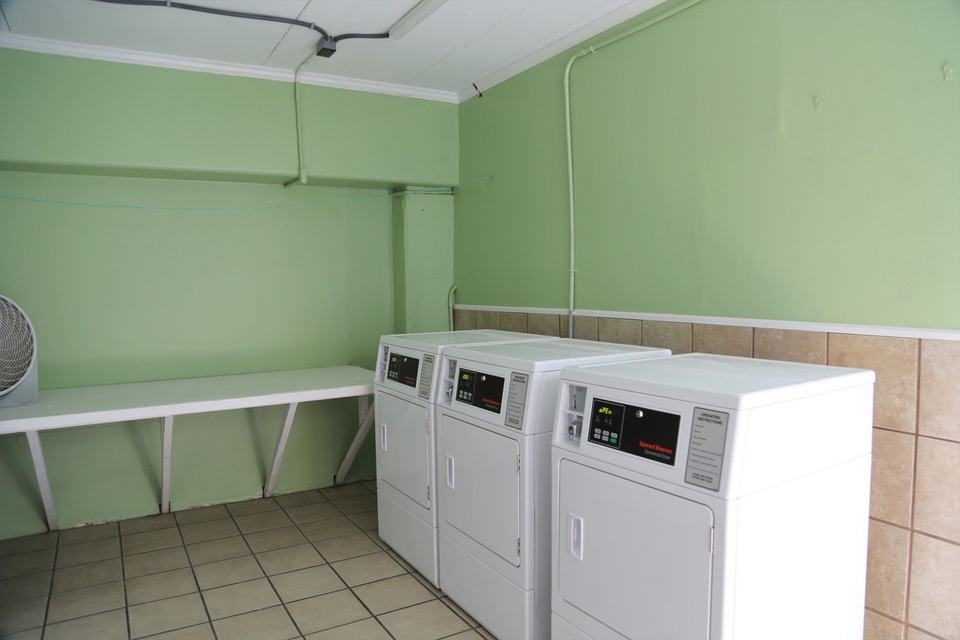 A laundry room with three stacked washing machines, a white shelf, and a fan.
