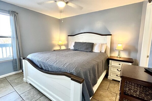 A bedroom with a bed, two bedside tables, a nightstand, a ceiling fan, and a window with curtains. - Ocean Reef 108 1 Bedroom Condo (Gulf Shores)