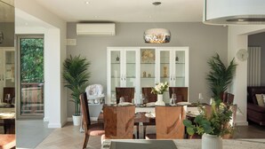 A modern dining area with a glass cabinet, wooden chairs, and a central table with a built-in induction cooktop.