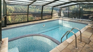 An indoor swimming pool with clear glass walls, a tiled floor, and a metal ladder.