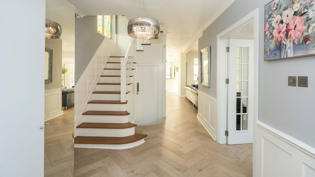 A staircase with wooden steps and white walls, leading to a hallway with a chandelier and a painting of flowers.