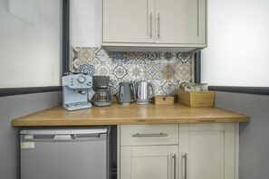 A compact kitchen with a dishwasher, a coffee maker, a kettle, and a wooden box on the counter.
