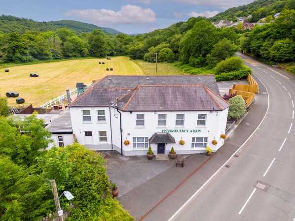A white building with "YNYSMEUDWY ARMS" signage, located beside a road with a grassy field and hills in the background. - Unique Exclusive Pub Sleeping up to 26 People (Pontardawe)