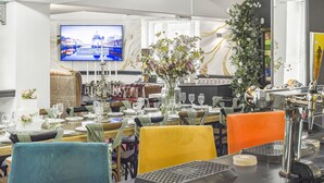 A dining area with tables set for a meal, a television displaying a cityscape, and a decorative floral arrangement. - Unique Exclusive Pub Sleeping up to 26 People (Pontardawe)
