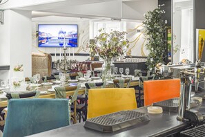 A dining area with tables set for a meal, a television displaying a cityscape, and a decorative floral arrangement.