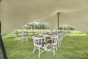 A tented outdoor dining area with white tables and chairs, surrounded by green grass.