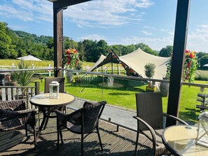 An outdoor patio with wicker furniture and a glass table, overlooking a grassy area with a tent and a small pond. - Unique Exclusive Pub Sleeping up to 26 People (Pontardawe)