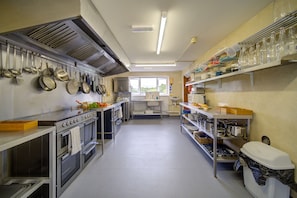 A kitchen with stainless steel appliances, hanging pots, and shelves with glassware.