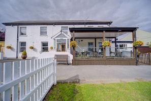 A white building with a covered patio area, a wooden deck, and a white fence. - Unique Exclusive Pub Sleeping up to 26 People (Pontardawe)