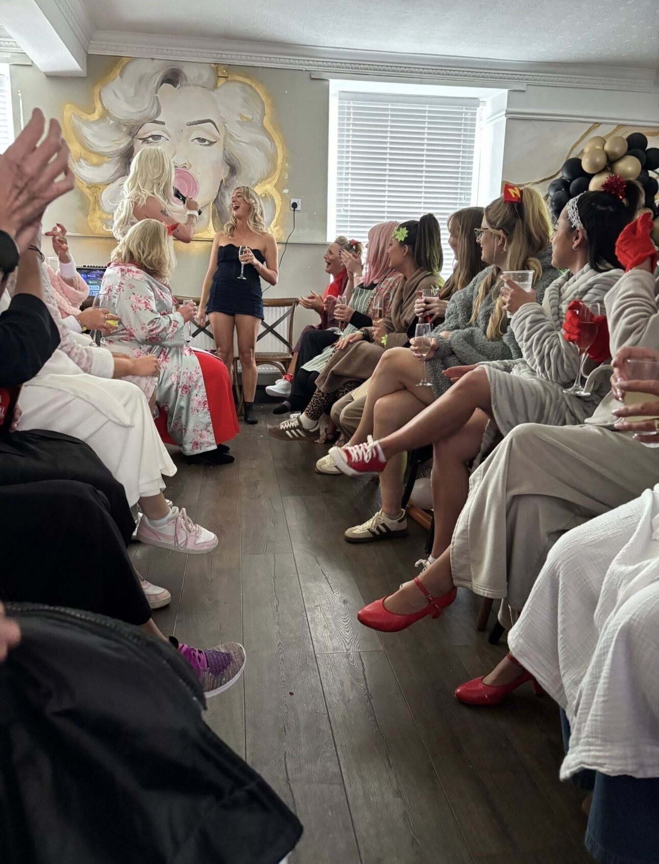 A group of people seated in a room with a wooden floor, engaged in a social event.
