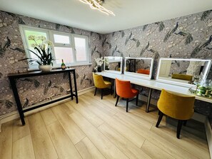 Una habitación con piso de madera, una mesa con una planta, dos sillas, un espejo y papel tapiz floral.