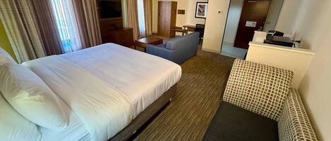 Una habitación de hotel con una cama grande, un sofá, un escritorio y una televisión.
