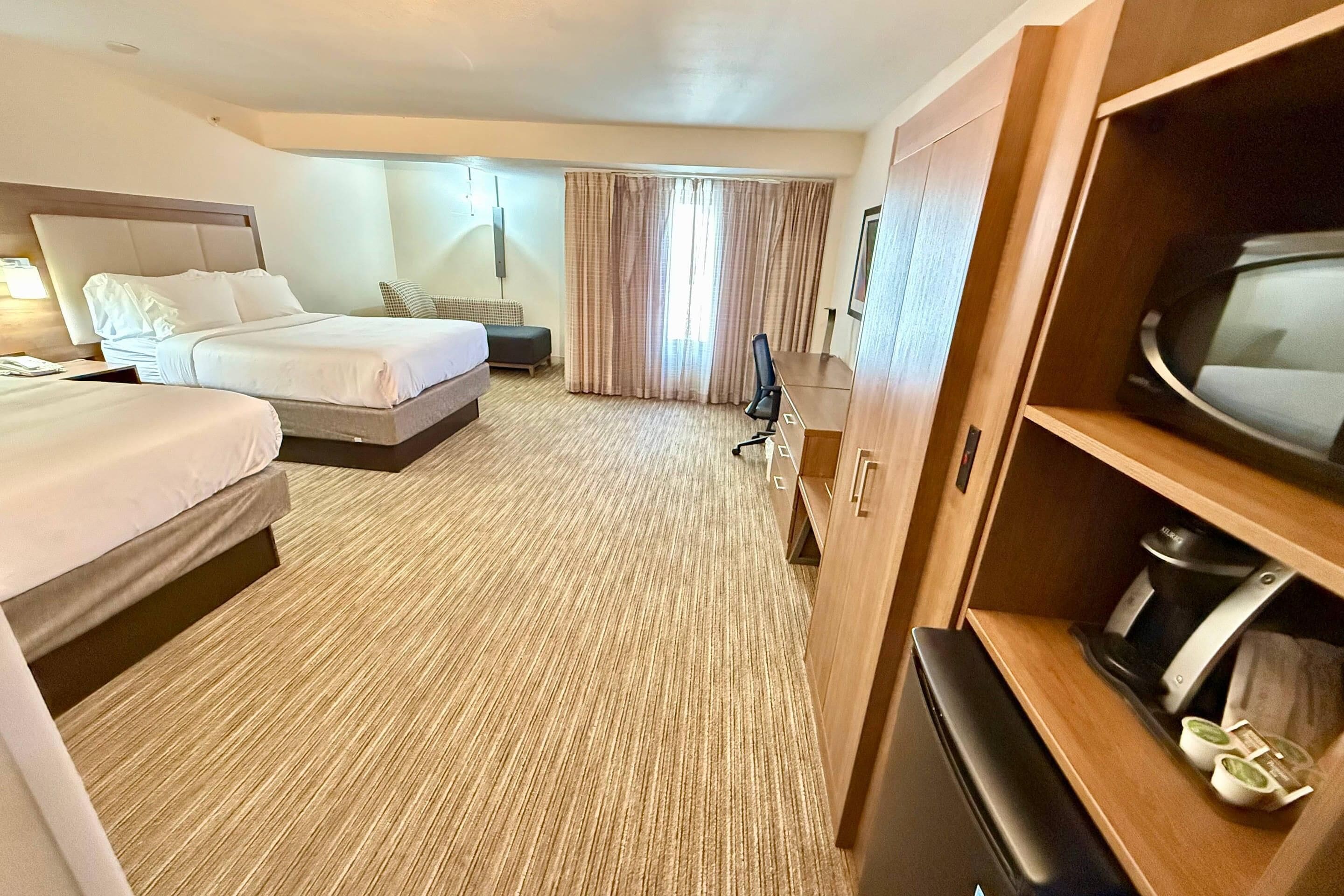 A hotel room with two beds, a desk, a television, and a coffee machine.