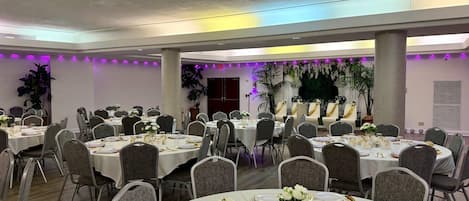 A banquet hall with round tables set for dining, featuring gold and white tableware, and surrounded by grey chairs.