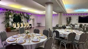 Un salón de banquetes con mesas redondas dispuestas para comer, rodeado de sillas.