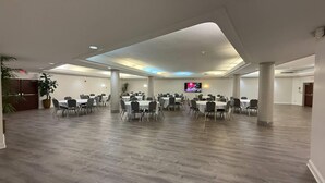 Un amplio y bien iluminado salón de conferencias con mesas y sillas redondas, un televisor de pantalla plana y suelo de madera.
